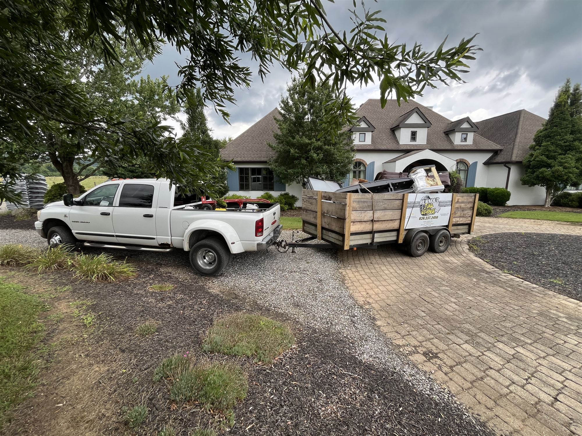 Truck and branded trailer loaded with junk in front of a large home