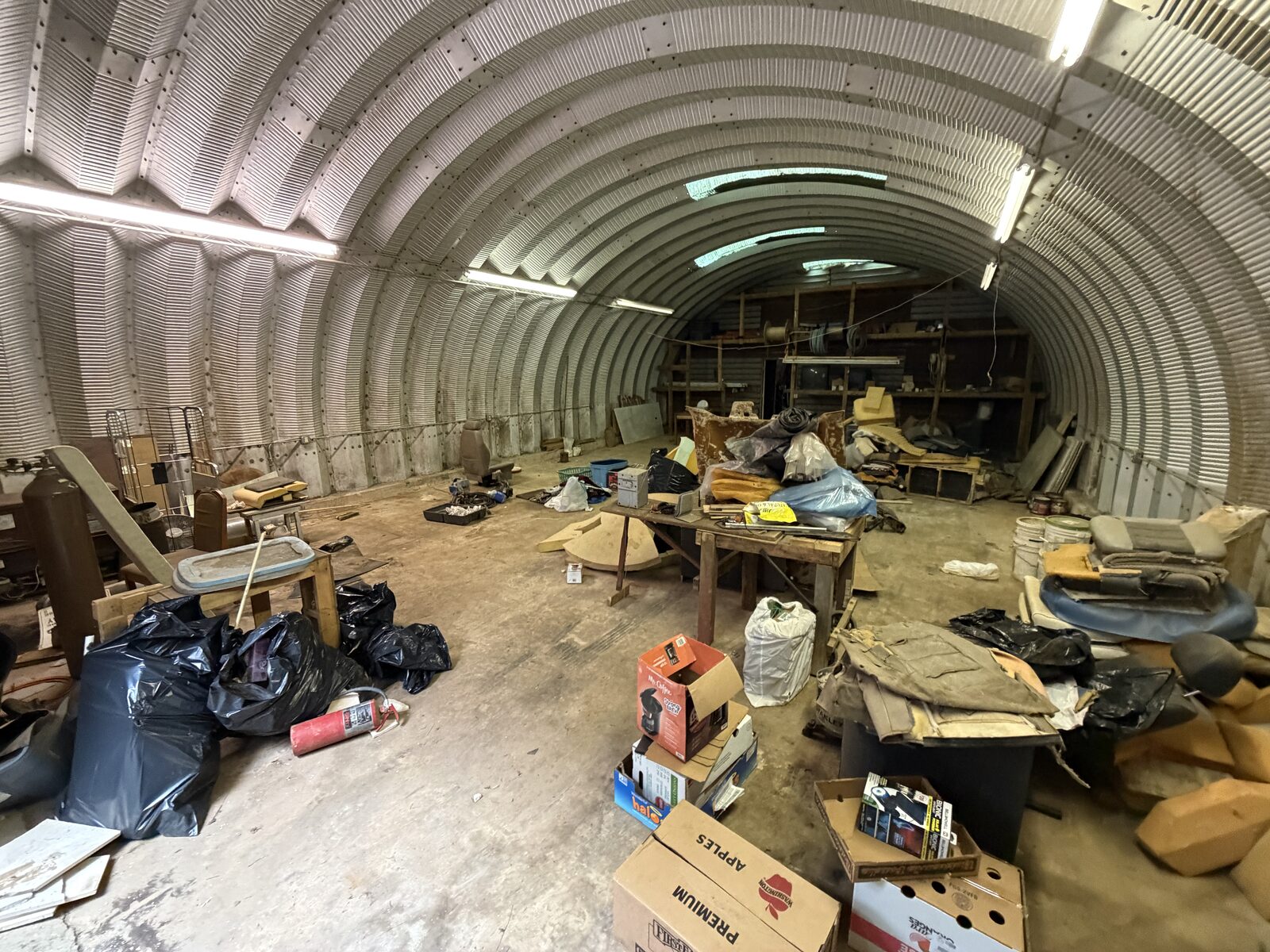 Metal arch workshop building packed with junk, bags and old furniture